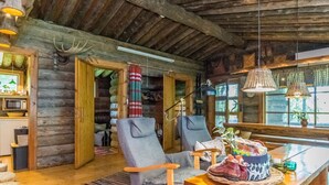 Ein rustikales Blockhaus-Interieur mit Holzwänden, einem Esstisch, zwei Stühlen, einer Küchenzeile und einem großen Fenster.