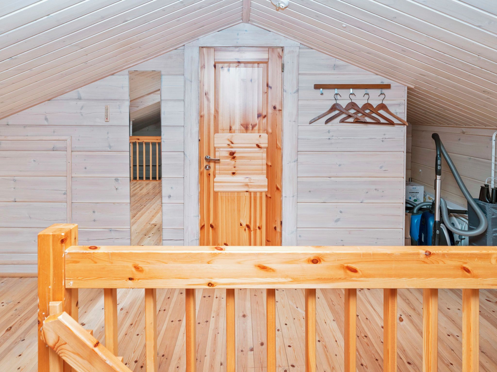 Un intérieur en bois avec un plafond en pente, une porte en bois, un porte-manteau et un aspirateur.
