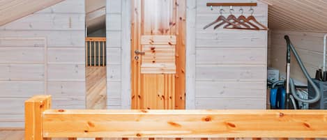Un interno in legno con soffitto spiovente, una porta in legno, un appendiabiti e un aspirapolvere.