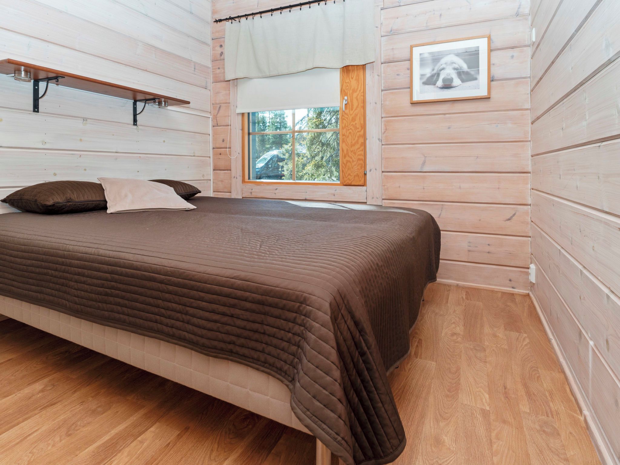 Una habitación con paneles de madera, una cama, una ventana y un cuadro en la pared.