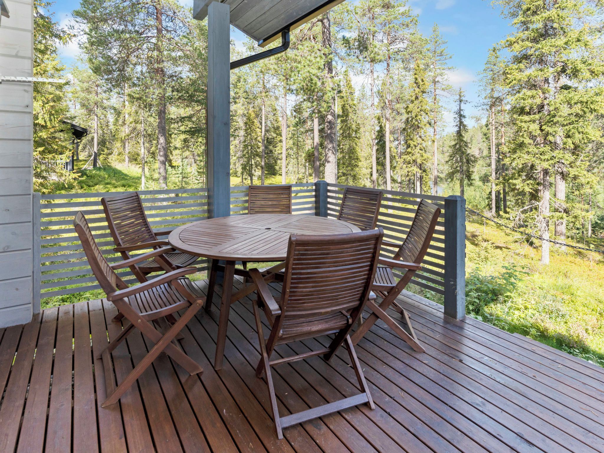 A wooden deck with a round table and chairs, surrounded by a wooden fence, overlooking a forested area.