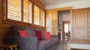 Ein modernes Wohnzimmer mit einem grauen Sofa, roten Kissen, einem Holztisch und einem Holzboden.