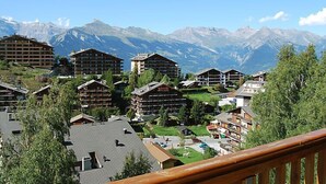 Ein Bergresort mit Chalet-Gebäuden, eine Skipiste und Blick auf schneebedeckte Berge.