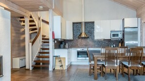 A modern kitchen with wooden flooring, a dining area with wooden chairs, and a staircase leading to an upper level.