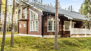A wooden cabin with a porch, surrounded by trees and a grassy area.