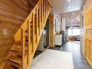 A wooden interior with a staircase leading to an upper level, a kitchen area with a refrigerator, and a seating area with a sofa. - Sini-ruka 1 by Interhome (Kuusamo)