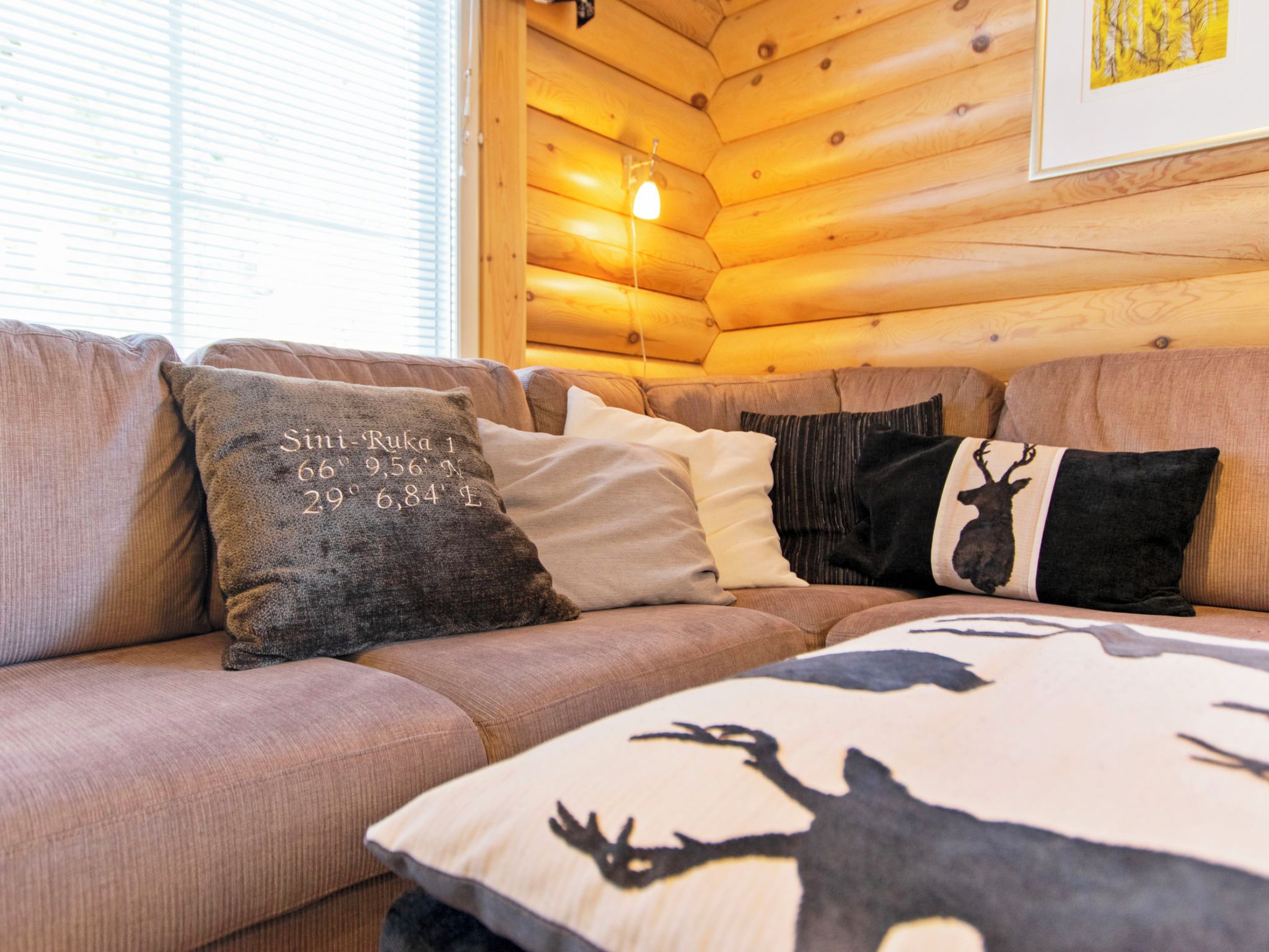A wooden cabin interior with a sofa and decorative pillows, including one with coordinates.