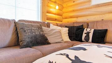 A wooden cabin interior with a sofa and decorative pillows, including one with coordinates.