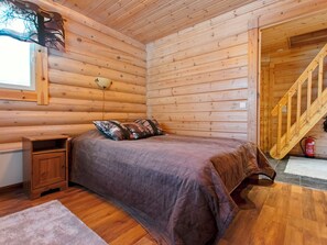 Ein Schlafzimmer in einer Blockhütte mit einem Bett, einem Nachttisch und einem Fenster mit Blick auf Bäume.