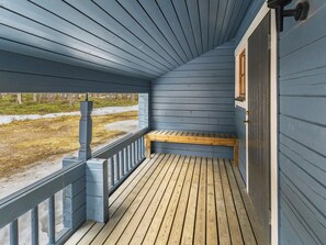 Une véranda couverte avec un banc en bois et une vue sur l’extérieur.