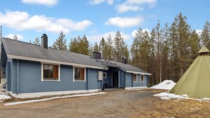 A two-story blue building with a gravel driveway and a tent in the foreground.