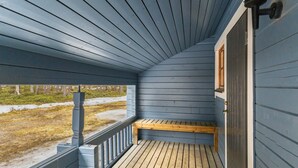 A covered porch with a wooden bench and a window, overlooking a snowy landscape.