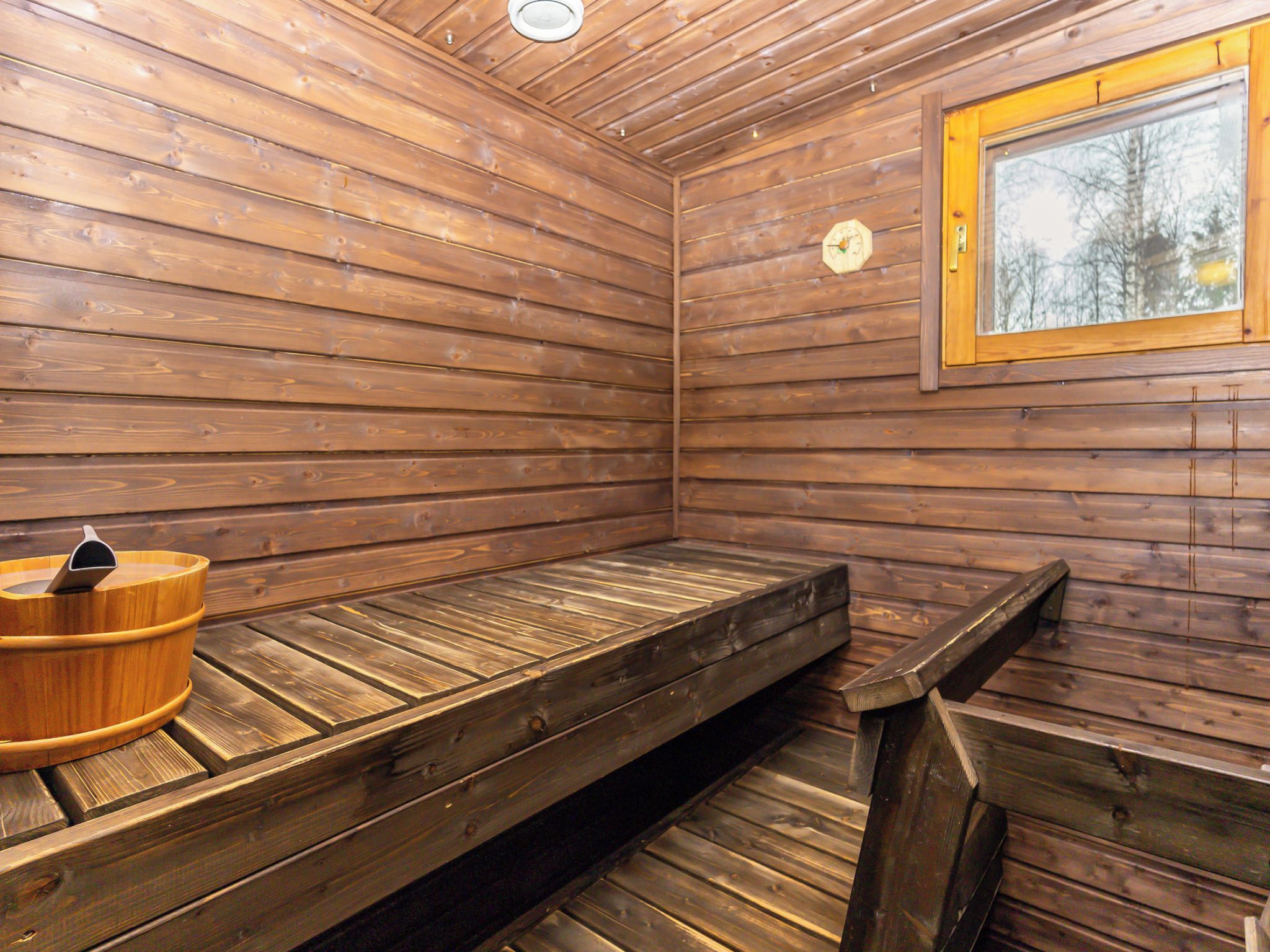 A sauna room with wooden walls, a bench, and a wooden bucket.