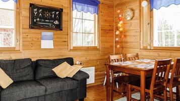 Interior acogedor de una cabaña con piso de madera, un sofá negro, una mesa de comedor con sillas y un reloj en la pared.