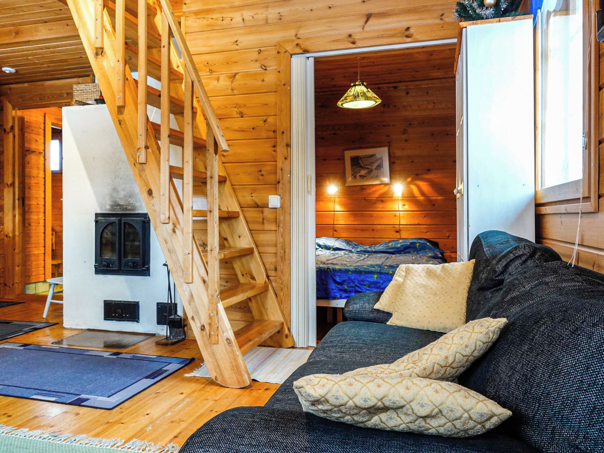 Interior acollidor d'una cabana amb una escala de fusta, un llit, un sofà i una llar de foc.