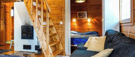 L’intérieur chaleureux d’un chalet avec un escalier en bois, un lit, un canapé et une cheminée.