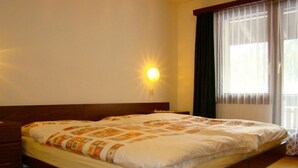 A neatly made bed with a patterned bedspread, a wooden headboard, and a wall-mounted light. - Apartment Mikado by Interhome (Saas-Fee)