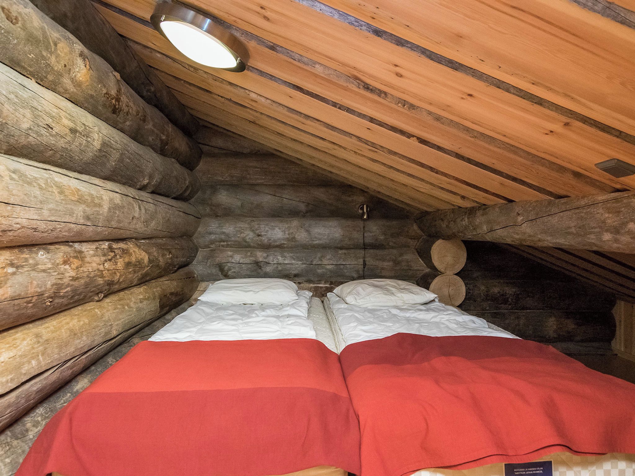 A log cabin room with a bed, a red blanket, and a ceiling light.