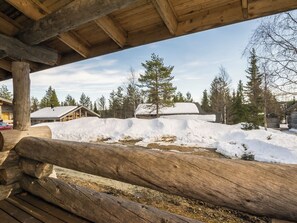 A wooden cabin with a snow-covered roof, surrounded by trees and a wooden fence.