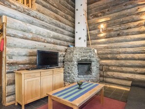 A log cabin interior with a stone fireplace, wooden furniture, and a television. - Tokka 1 by Interhome (Kuusamo)