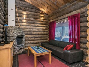 A log cabin interior with a stone fireplace, a sofa, a table, and a window with curtains.