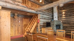 Ein rustikales Blockhaus-Interieur mit Essbereich, Kamin und einer Wendeltreppe.