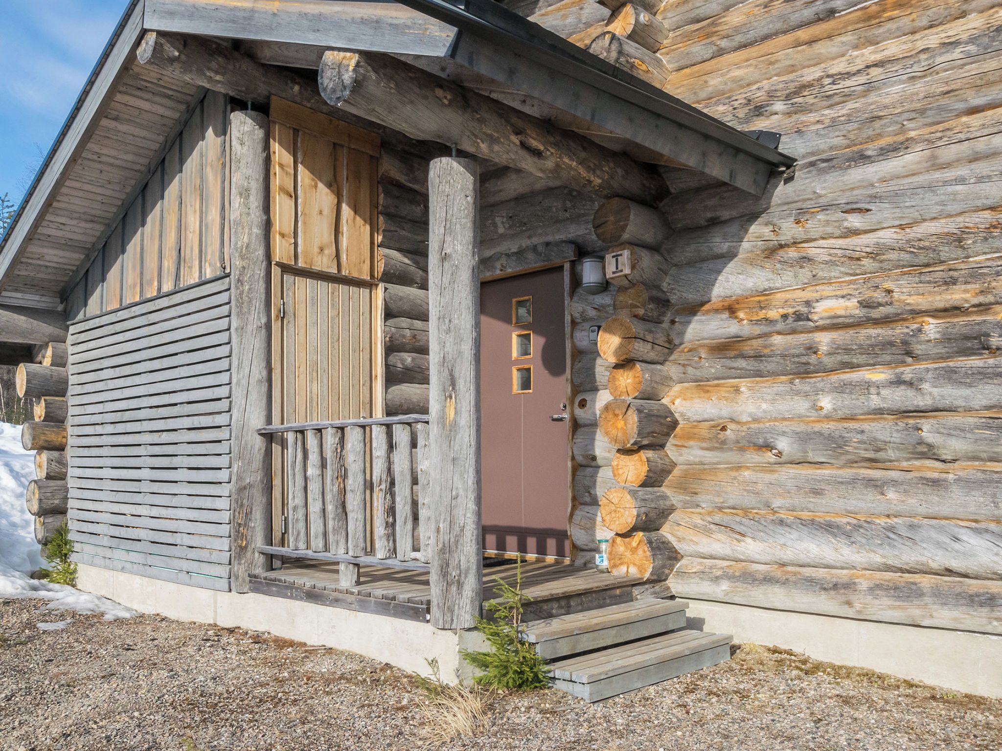 A log cabin with a wooden door, a small porch, and a concrete foundation.