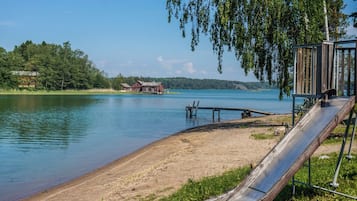 Une scène au bord du lac avec un toboggan en bois, une jetée et un bâtiment rouge au loin.