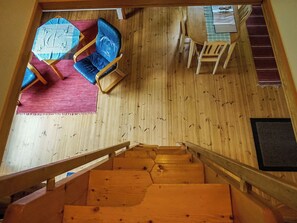 A wooden staircase leading to a room with a wooden floor, a blue sofa, a red rug, and a table with chairs. - Nokikana 7 by Interhome (Parainen)