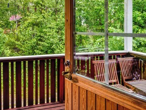 A wooden deck with a glass door leading to a view of a lush green forest.