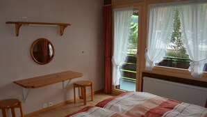 A bedroom with a bed, a desk, two stools, a mirror, and a window with curtains. - Mösli (Zimmerli) by Interhome (Zweisimmen)