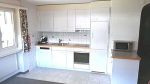 A compact kitchen with white cabinets, a microwave, a dishwasher, and a window with curtains.