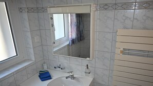 A bathroom with a white sink, a mirror, a window, and a towel rack.