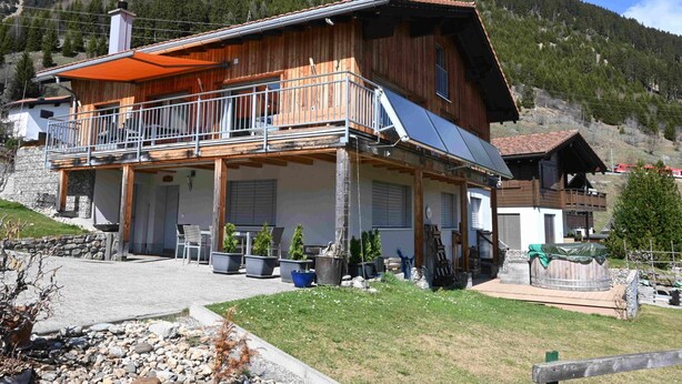 A wooden chalet with a balcony, solar panels, and a stone wall.