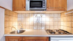 Una cocina compacta con gabinetes de madera, un lavamanos de acero inoxidable, un microondas integrado y una estufa.