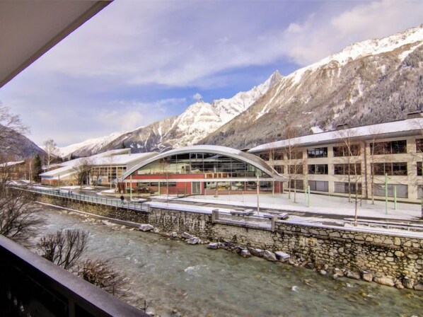 A modern building with a curved roof, a stone wall, and a river in front.