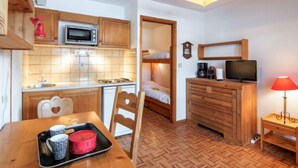 Cocina compacta con microondas, estufa y lavamanos. Cuenta con una mesa de comedor con sillas y una pequeña zona de TV con una lámpara.
