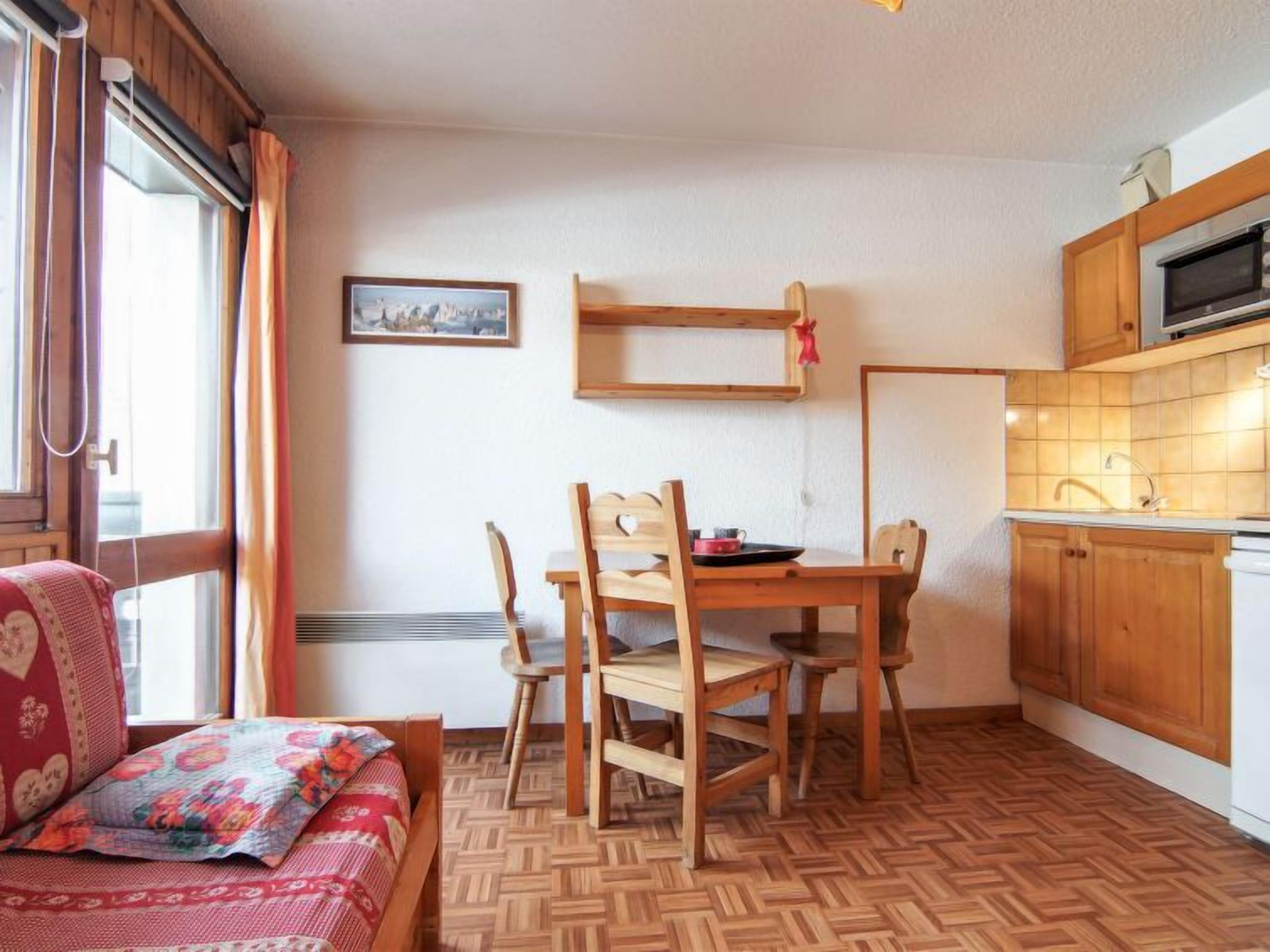 A cozy room with a wooden dining table, chairs, a sofa, and a kitchen area with wooden cabinets and a microwave.