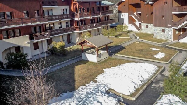 Un hotel de varios pisos con balcones, una zona de estar al aire libre techada y vistas a montañas nevadas.