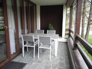 A covered patio area with a table and chairs, a wooden deck, and a view of the outdoors.