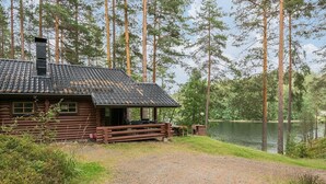 A rustic cabin with a gravel driveway, surrounded by tall pine trees and a lake. - Salmela by Interhome (Puumala)