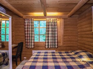 A cabin room with a bed, a chair, a window with curtains, and a view of the forest.