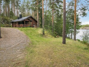 A log cabin with a gravel path leading to it, surrounded by a forest and a lake.