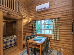 A log cabin interior with a dining table, chairs, a window with curtains, and an air conditioning unit.