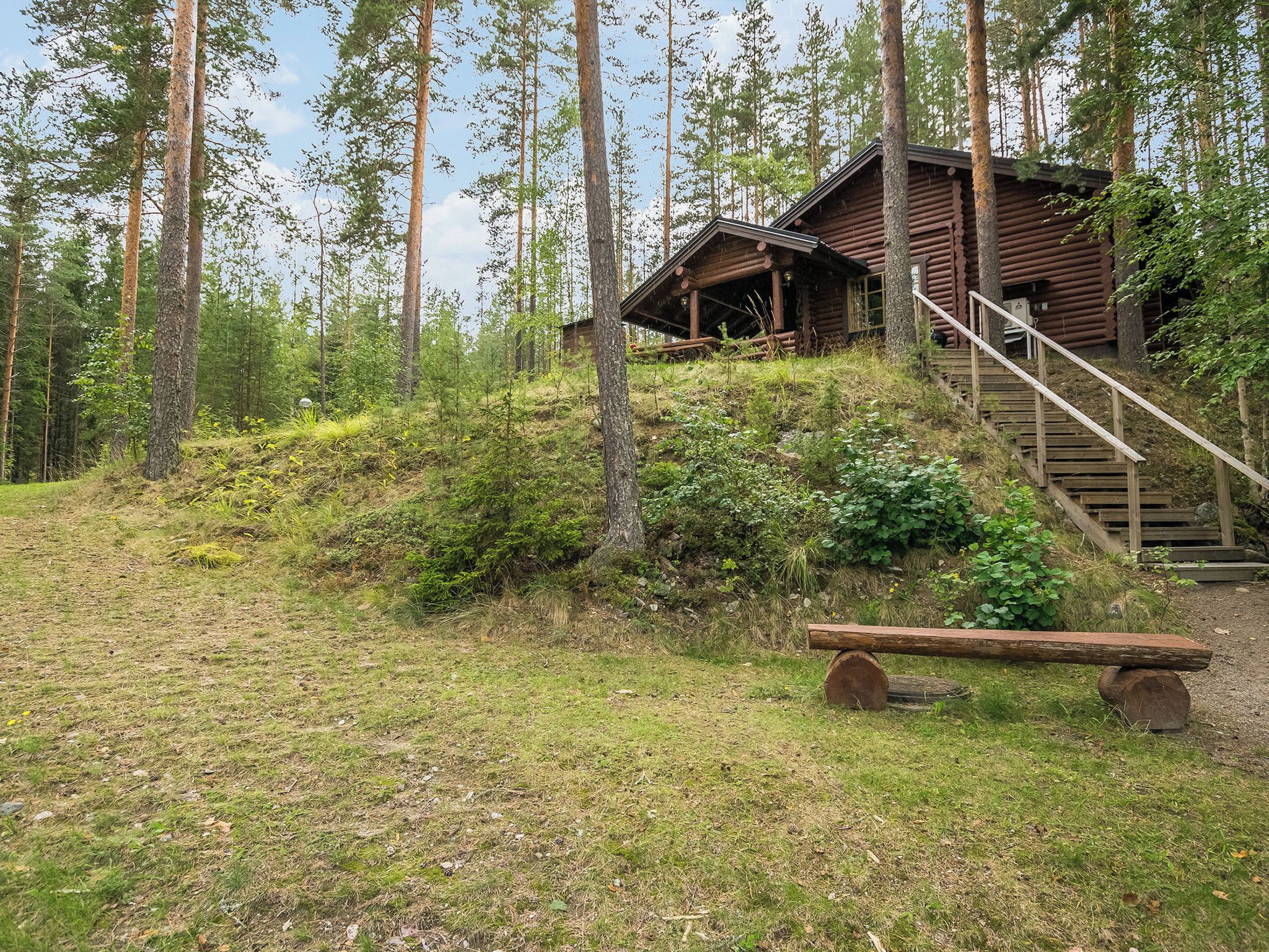 A rustic cabin with a wooden staircase leading up to a porch, surrounded by a forested area.