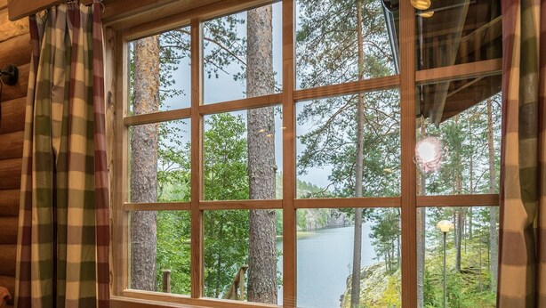 A cabin with a large window offering a view of a forest and a lake. - Salmela by Interhome (Puumala)