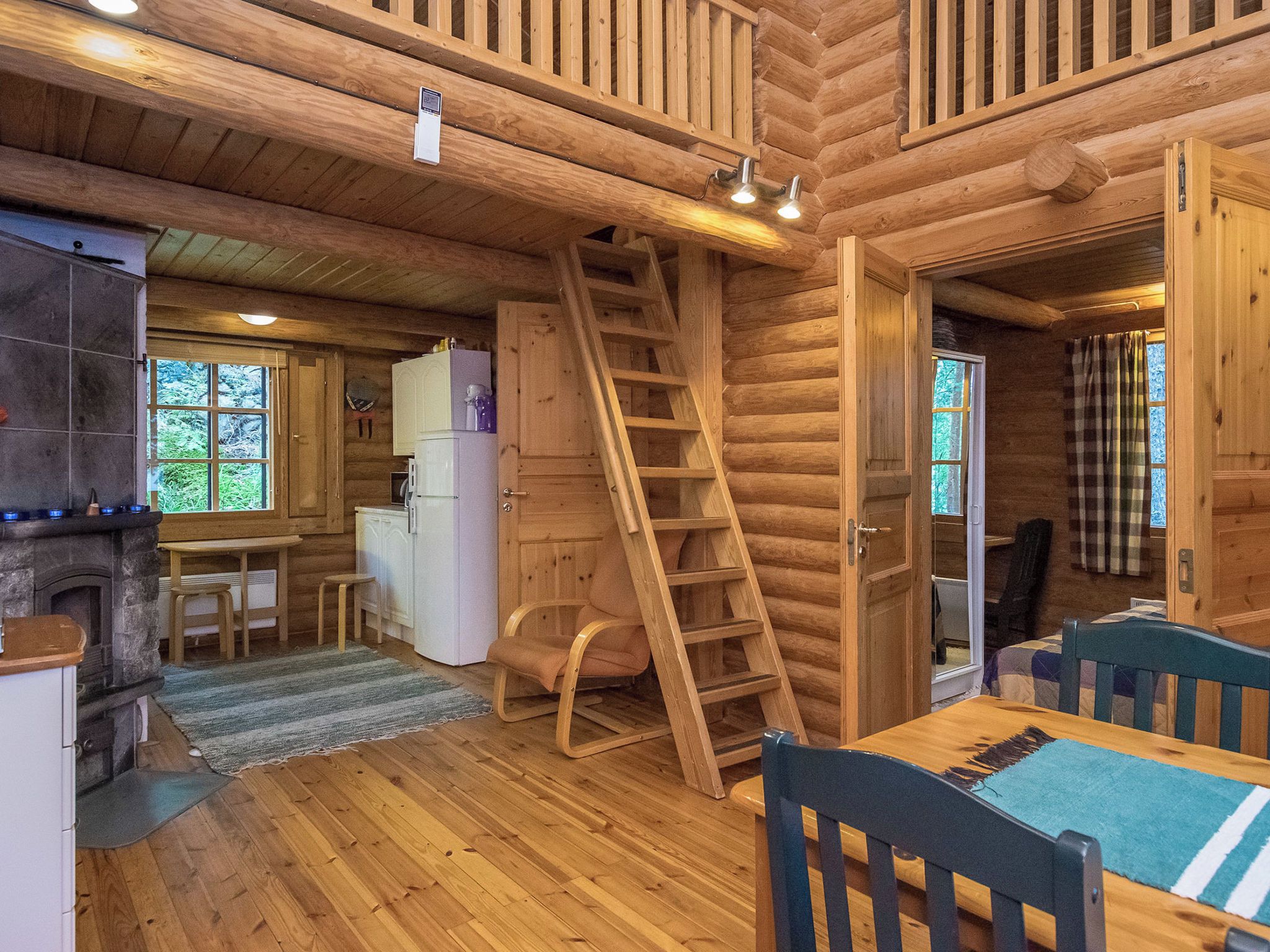 A log cabin interior with a kitchen, dining area, and a loft bedroom.