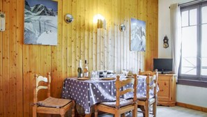 A dining area with wooden panel walls, a table set for four, and a television on a wooden cabinet. - Le Savoisien by Interhome (Chamonix)