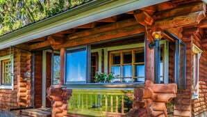 A log cabin with a porch, large windows, and a wooden staircase leading to the entrance.