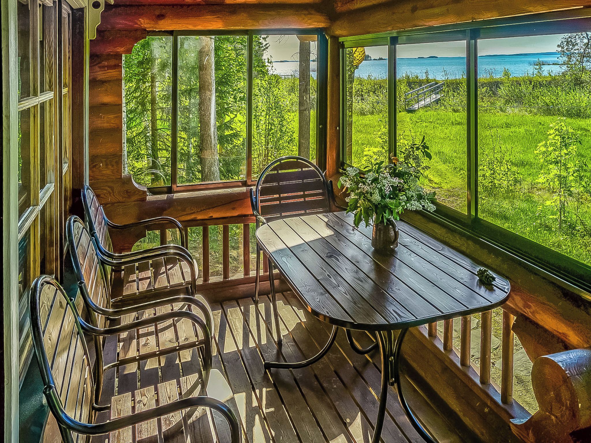A wooden deck with a table and chairs, overlooking a lush green landscape and a body of water.